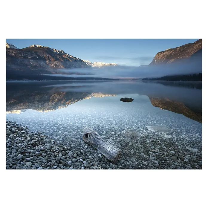 Papermoon Premium collection Fototapete Bohinjs Ruhigkeit - B x H: 350 x 260 cm, Vlies - Ein ruhiger See spiegelt schneebedeckte Berge wider, mit klarem Wasser und einem Treibholzstück im Vordergrund. Die friedliche Landschaft lädt zum Verweilen ein.