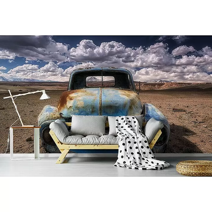 Papermoon Premium collection Fototapete Eindringen - B x H: 300 x 223 cm, Vlies - Holzsofa mit grauen Kissen und gepunkteter Decke, weiße Lampe-Beistelltisch und Flechtpouf vor Rost-Lkw-Wandbild.