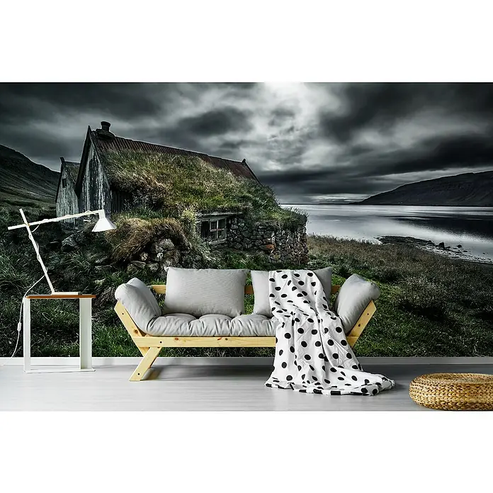 Papermoon Premium collection Fototapete Rasen und Steine - B x H: 250 x 186 cm, Vlies - Das Bild zeigt ein modernes Sofa mit Kissen und einer gepunkteten Decke vor einer Tapete mit einem alten Haus in der Landschaft.
