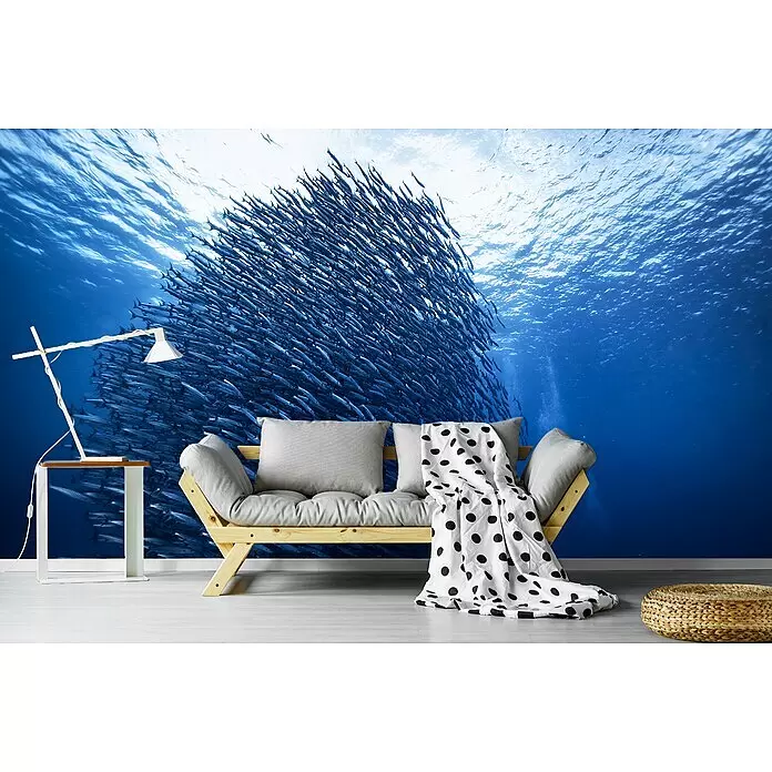 Papermoon Premium collection Fototapete Massengigant - B x H: 500 x 280 cm, Vlies - Ein helles Holzfuton mit grauen Kissen, einer gepunkteten Decke, einer minimalistischen Lampe auf einem Beistelltisch und einem geflochtenen Pouf in einem Raum.