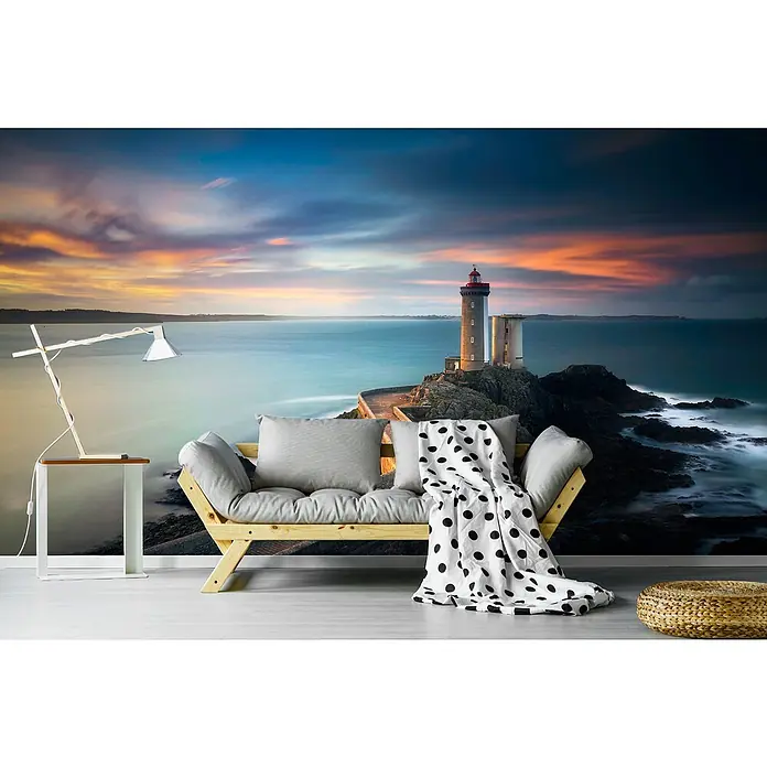 Papermoon Premium collection Fototapete Phare du petit minou - B x H: 400 x 260 cm, Vlies - Wohnzimmer mit einer Couch, einem Beistelltisch und einem Hocker vor einer Fototapete mit Leuchtturm bei Sonnenuntergang.