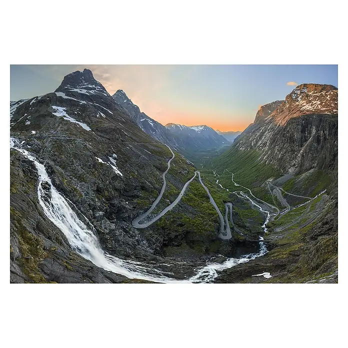 Papermoon Premium collection Fototapete Trollstigen - B x H: 500 x 280 cm, Vlies - Serpentinenstraße schlängelt sich durch eine dramatische Berglandschaft mit Wasserfall und schneebedeckten Gipfeln im Abendlicht.