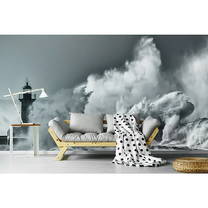 Papermoon Premium collection Fototapete Wirbelwind - B x H: 400 x 260 cm, Vlies - Ein Wohnzimmer mit einer Wandtapete, die einen Leuchtturm und tosende Wellen zeigt, sowie einem Holzbettsofa und einem Hocker.