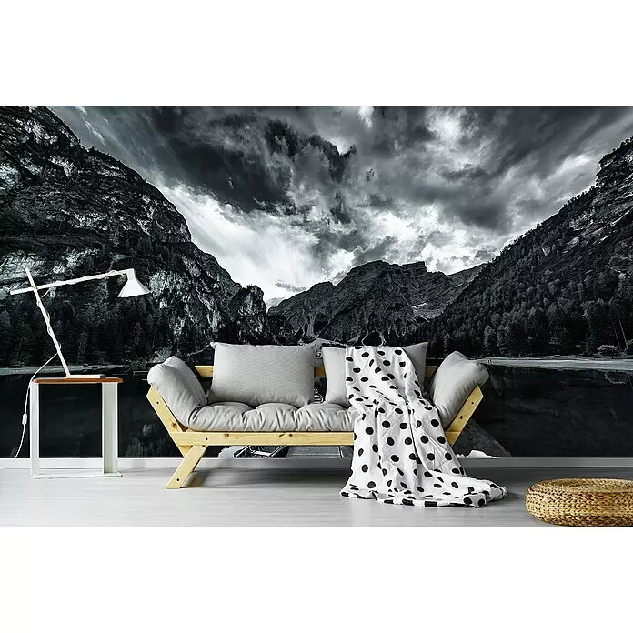 Papermoon Premium collection Fototapete Braies 'Graustufen' - B x H: 400 x 260 cm, Vlies - Helles Holzsofa mit grauen Kissen in einem Raum mit Naturwandbild. Eine Lampe und ein geflochtener Pouf sind in der Nähe.