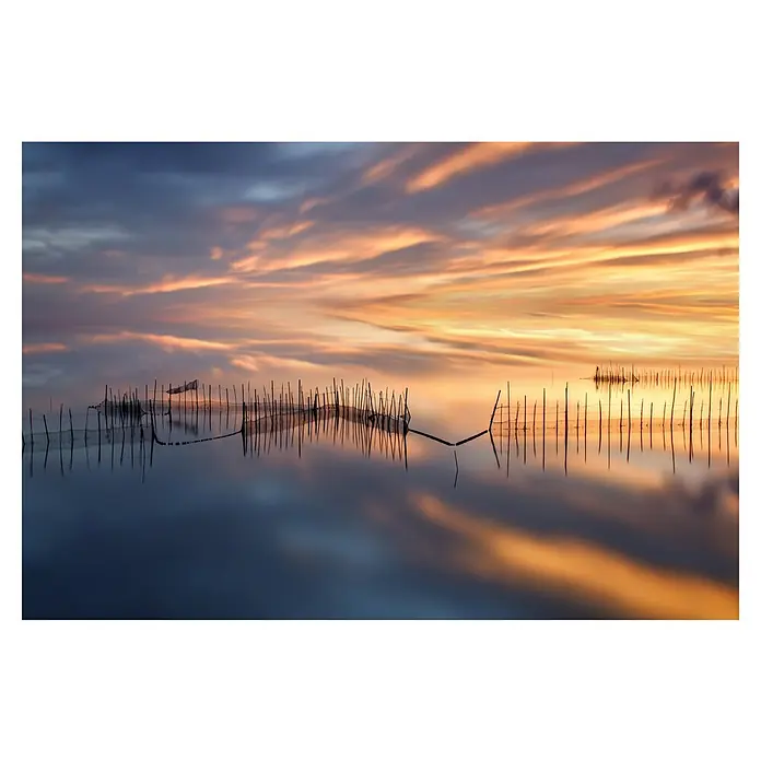 Papermoon Premium collection Fototapete Fishnetten - B x H: 300 x 223 cm, Vlies - Ruhige Aufnahme eines Sees bei Sonnenuntergang mit Holzpfählen, die sich im Wasser spiegeln und eine friedliche, natürliche Atmosphäre schaffen.