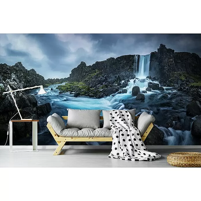 Papermoon Premium collection Fototapete Zwischen Kontinenten - B x H: 350 x 260 cm, Vlies - Helles Holzsofa mit grauen Kissen und einer gepunkteten Decke vor einer Wasserfall-Wandtapete.