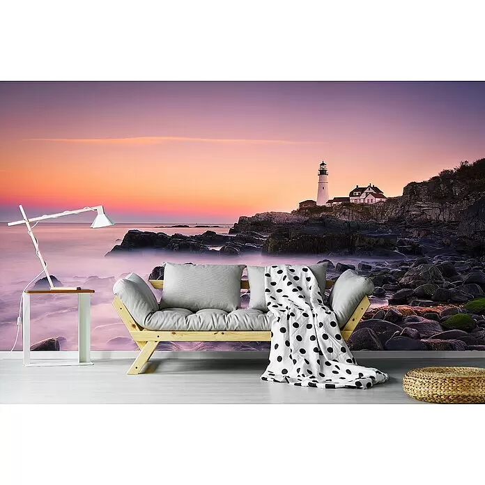 Papermoon Premium collection Fototapete Portland Scheinwerfer - B x H: 250 x 186 cm, Vlies - Ein helles Holz-Futonsofa mit grauen Kissen, gepunkteter Decke, weißem Beistelltisch mit Lampe und geflochtenem Pouf in einem Raum mit Wandbild.