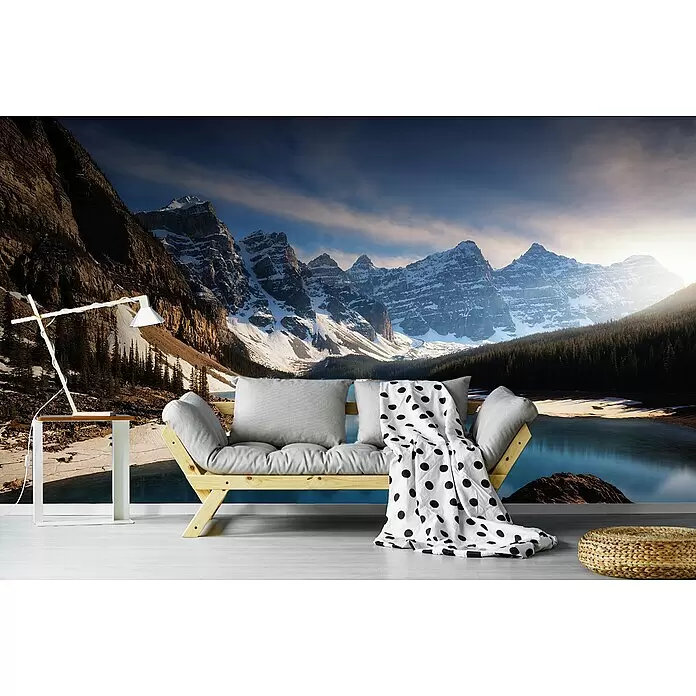 Papermoon Premium collection Fototapete Berge- und Seenlandschaft - B x H: 250 x 186 cm, Vlies - Ein Holz-Tagesbett mit hellgrauen Kissen und einer gepunkteten Decke in einem Raum mit Berg-See-Wandgemälde.