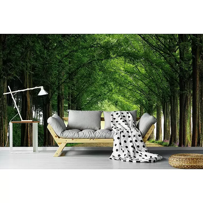 Papermoon Premium collection Fototapete Metasequoiaroad - B x H: 250 x 186 cm, Vlies - Modernes Holzsofa mit grauen Kissen und gepunkteter Decke, neben weißem Beistelltisch mit minimalistischer Lampe, in einem Raum mit lebendiger Waldtapete.