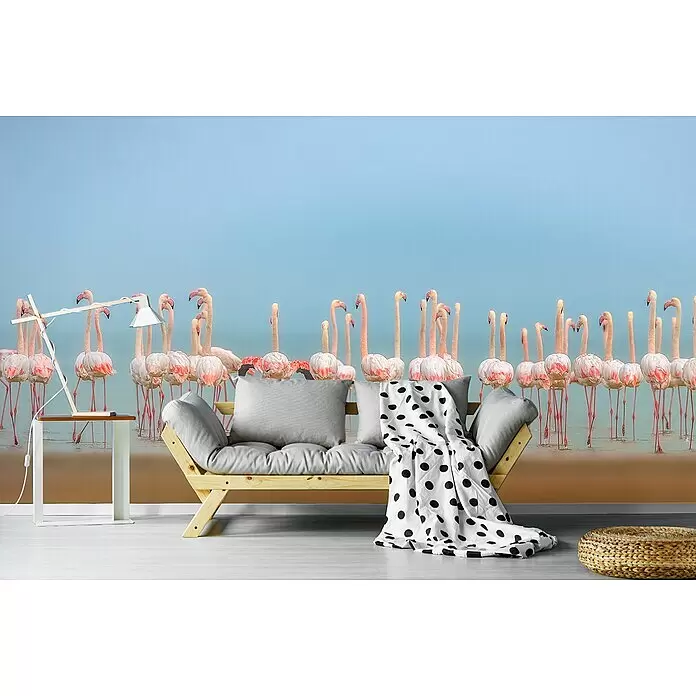 Papermoon Premium collection Fototapete Bläser - B x H: 300 x 223 cm, Vlies - Helles Holz-Futonsofa mit grauen Kissen und schwarz gepunkteter Decke, in einem Raum mit Flamingo-Wandbild.