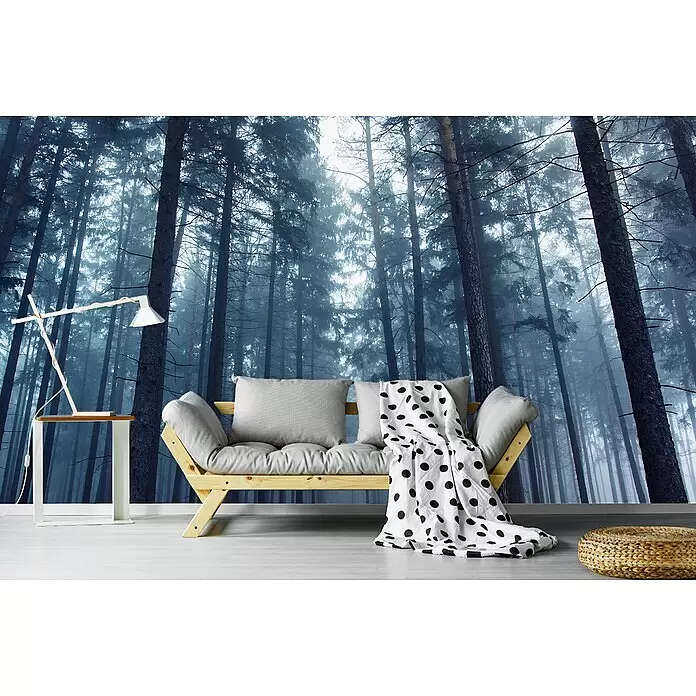 Papermoon Premium collection Fototapete Geheimnisvoll nebliger Wald - B x H: 250 x 186 cm, Vlies - Ein helles Holzsofa mit grauen Kissen und gepunkteter Decke, daneben eine weiße Lampe auf einem Beistelltisch und ein gewebter Pouf.
