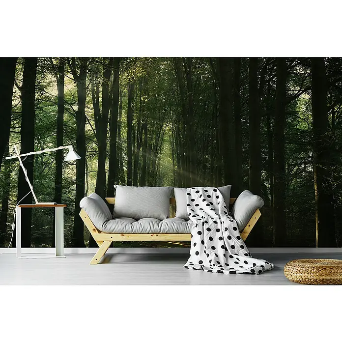 Papermoon Premium collection Fototapete Sonnenstrahlen im Wald - B x H: 250 x 186 cm, Vlies - Wohnzimmer mit einem hellen Holzsofa mit Kissen und einer gepunkteten Decke vor einer Waldtapete und einer Nachttischlampe.