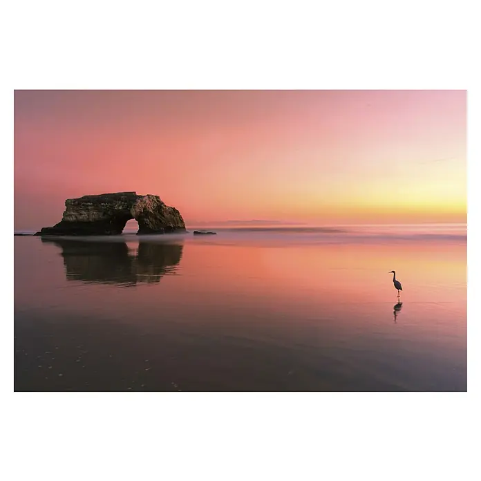 Papermoon Premium collection Fototapete Sonnenuntergang Naturbrücke - B x H: 400 x 260 cm, Vlies - Ein wunderschöner Sonnenuntergang am Strand mit einem Felsenbogen und einem Reiher im ruhigen Wasser, der die friedliche Szene hervorhebt.