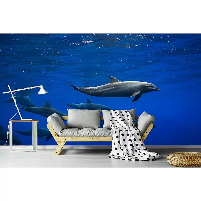 Papermoon Premium collection Fototapete Delphine I - B x H: 250 x 186 cm, Vlies - Holzsofa mit hellgrauen Kissen und schwarz-weiß gepunkteter Decke in einem Raum mit Delfin-Wandbild.