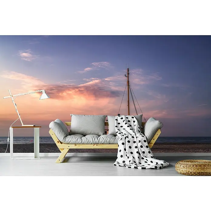 Papermoon Premium collection Fototapete Jammerbugten - B x H: 400 x 260 cm, Vlies - Eine stilvolle Couch mit Kissen und einer gepunkteten Decke vor einem wunderschönen Strandhintergrund. Eine Lampe und ein Hocker ergänzen das Bild.