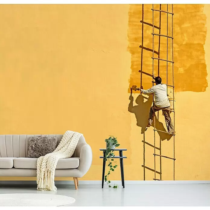 Papermoon Premium collection Fototapete Der Anstreicher - B x H: 300 x 223 cm, Vlies - Ein Wohnzimmer mit Sofa und Pflanze vor einer leuchtend gelben Wand, an der ein Maler auf einer Strickleiter eine dunklere Farbe aufträgt.