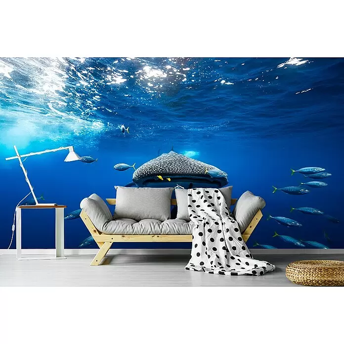 Papermoon Premium collection Fototapete Walhai Schule Bonito - B x H: 400 x 260 cm, Vlies - Holzbettsofa mit grauen Kissen und gepunkteter Decke, weißer Beistelltisch mit Lampe und geflochtener Pouf in einem Raum mit Unterwasserwandbild.