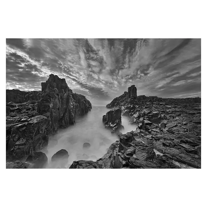 Papermoon Premium collection Fototapete Tor zum Himmel - B x H: 350 x 260 cm, Vlies - Mystische Schwarzweißaufnahme von dramatischen Klippen, die von Meer umspült werden, unter einem ausdrucksstarken Himmel.