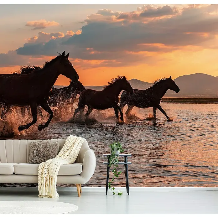 Papermoon Premium collection Fototapete Wasserpferde - B x H: 250 x 186 cm, Vlies - Wohnraum mit Pferde-Fototapete, die eine Herde im Sonnenuntergang zeigt, kombiniert mit beigem Sofa, Kissen, Überwurf und Beistelltisch mit Pflanze.