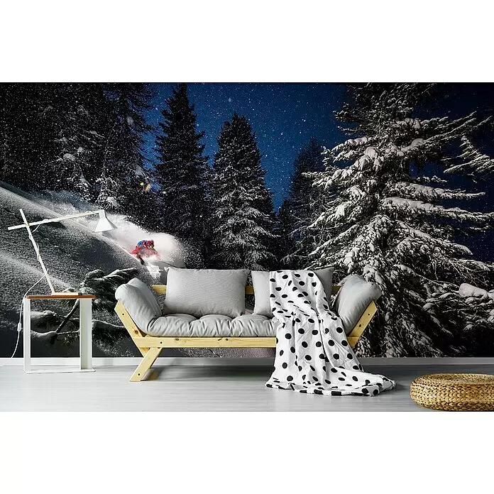 Papermoon Premium collection Fototapete Skipiste - B x H: 450 x 280 cm, Vlies - Ein Holzsofa mit grauen Kissen und einer gepunkteten Decke steht neben einem weißen Beistelltisch mit Lampe und einem geflochtenen Pouf auf hellem Boden.