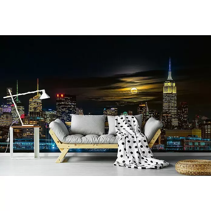 Papermoon Premium collection Fototapete New York City - B x H: 250 x 186 cm, Vlies - Helles Holzfutonsofa mit grauen Kissen und einer gepunkteten Decke in einem Raum mit nächtlicher Stadtskyline als Wandbild.