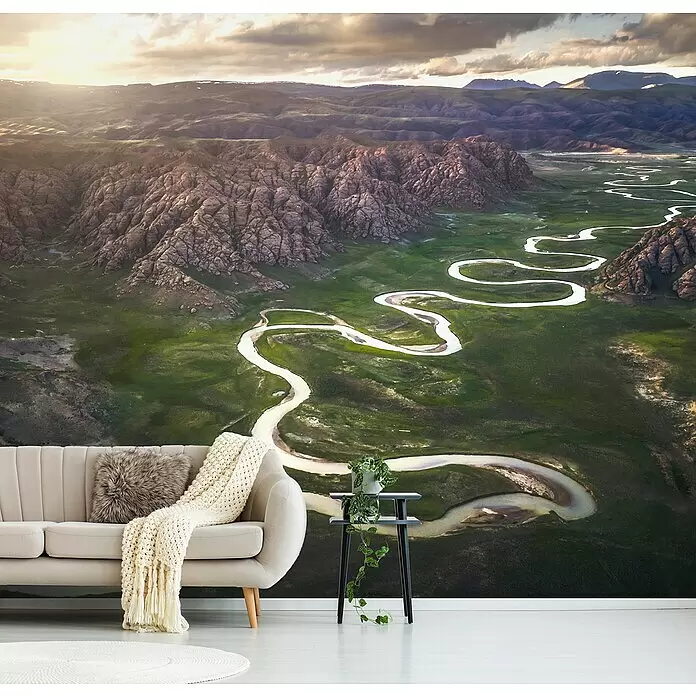 Papermoon Premium collection Fototapete 18 Biegungen der Wasserstraße - B x H: 350 x 260 cm, Vlies - Ein fotorealistisches Wandbild zeigt einen sich schlängelnden Fluss durch eine bergige Landschaft hinter einem beigen Sofa.