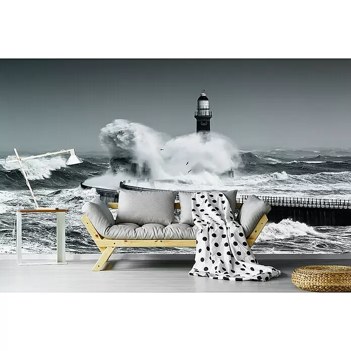 Papermoon Premium collection Fototapete Macht des Meeres - B x H: 500 x 280 cm, Vlies - Holzsofa mit grauen Kissen und schwarz-weiß gepunkteter Decke in einem Raum mit dramatischem Leuchtturm-Wandbild.