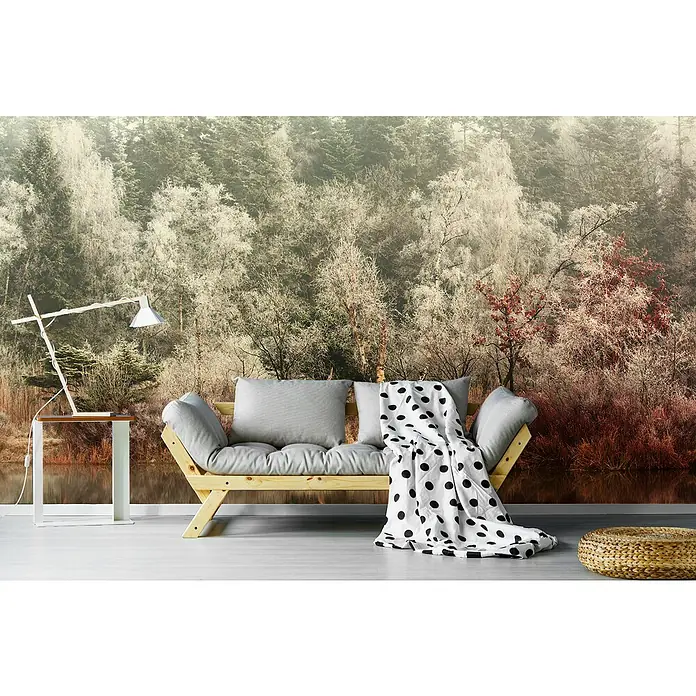 Papermoon Premium collection Fototapete Gefroren - B x H: 450 x 280 cm, Vlies - Ein gemütliches Wohnzimmer mit einer stilvollen Couch, einer Lampe und einem dekorativen Hocker vor einer beeindruckenden Waldtapete.