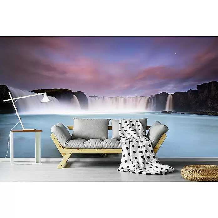 Papermoon Premium collection Fototapete Godafoss und Mond - B x H: 500 x 280 cm, Vlies - Hölzernes Futonsofa mit grauen Kissen und einer gepunkteten Decke, platziert in einem Raum mit großer Wasserfall-Wandmalerei.