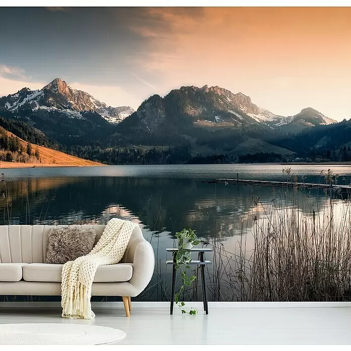 Papermoon Premium collection Fototapete Magische Stimmung Schwarzsee - B x H: 250 x 186 cm, Vlies - Ein gemütliches beiges Sofa mit Strickdecke und Beistelltisch mit Pflanze, vor einem Wandbild mit Bergsee.