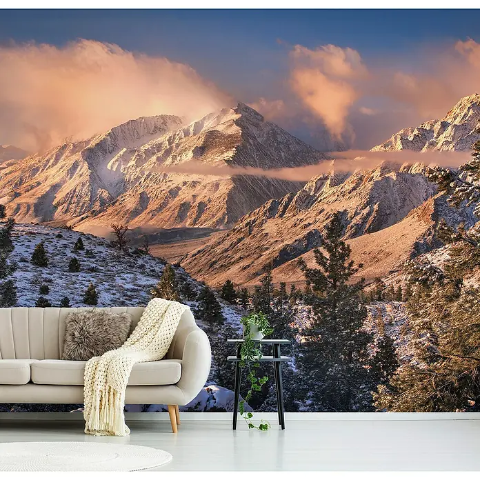 Papermoon Premium collection Fototapete Berglicht - B x H: 500 x 280 cm, Vlies - Wohnzimmer mit einem Sofa, einem Beistelltisch und einer Tapete mit Berglandschaft. Die Tapete zeigt schneebedeckte Berge bei Sonnenaufgang.