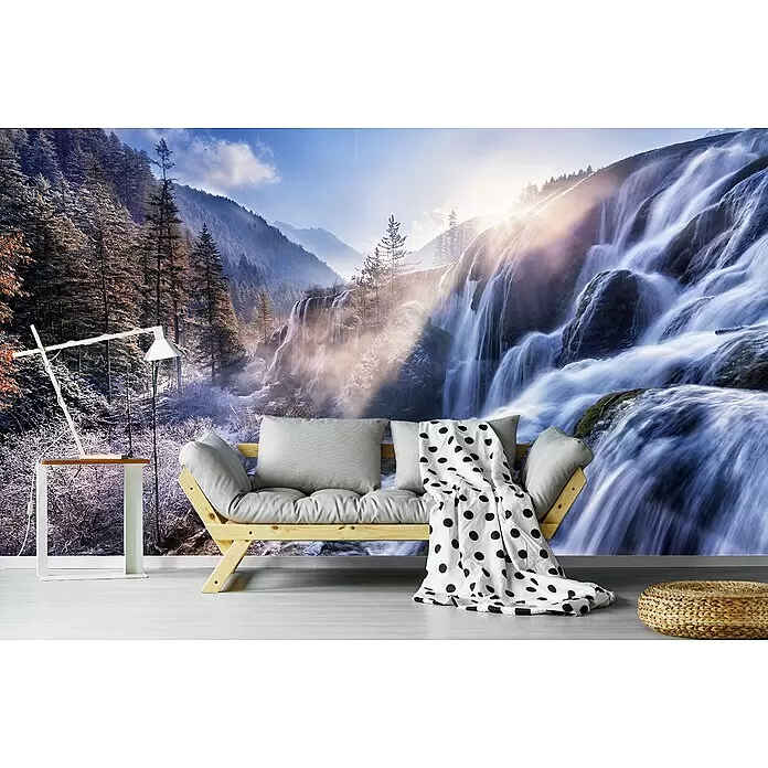 Papermoon Premium collection Fototapete Berglandschaft - B x H: 250 x 186 cm, Vlies - Ein Holzsofa mit hellgrauen Kissen und einer gepunkteten Decke, ein weißer Beistelltisch mit Lampe und ein geflochtener Pouf in einem Raum.