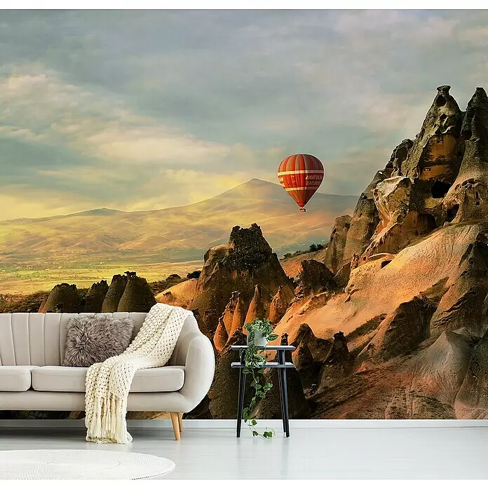 Papermoon Premium collection Fototapete Cappadocia - B x H: 500 x 280 cm, Vlies - Großes Wandgemälde zeigt einen Heißluftballon über einer felsigen Wüstenlandschaft hinter einem beigen Sofa.