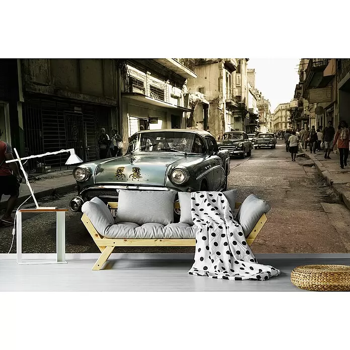 Papermoon Premium collection Fototapete Alte Havanna-Straße - B x H: 450 x 280 cm, Vlies - Hellgraues Holzsofa mit gepunkteter Decke, weißem Beistelltisch und geflochtenem Pouf in einem Raum mit Straßenwandbild.