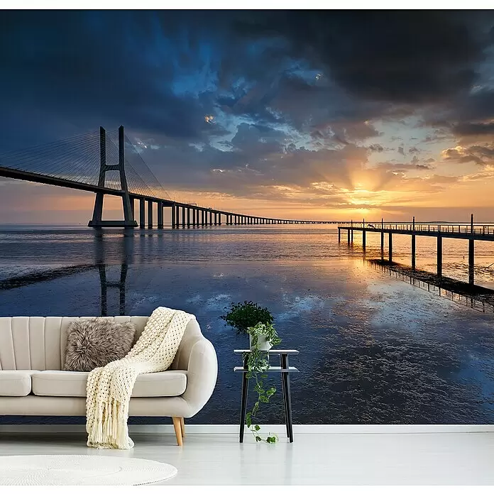 Papermoon Premium collection Fototapete Zwei Stege ins Meer - B x H: 250 x 186 cm, Vlies - Helles beiges Sofa mit grauem Kissen und Strickdecke, neben schwarzem Beistelltisch mit Pflanze, vor einer Wandmalerei.