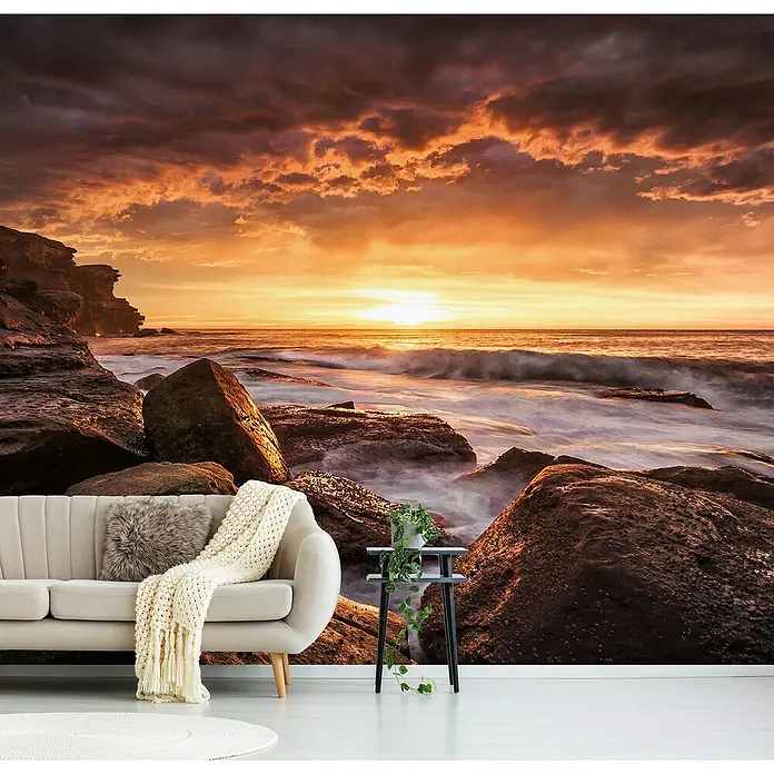 Papermoon Premium collection Fototapete Kapslöcher - B x H: 500 x 280 cm, Vlies - Ein stilvolles Wohnzimmer mit einer Fototapete, die einen atemberaubenden Sonnenuntergang über einer felsigen Küste zeigt. Die Tapete verleiht dem Raum Atmosphäre.