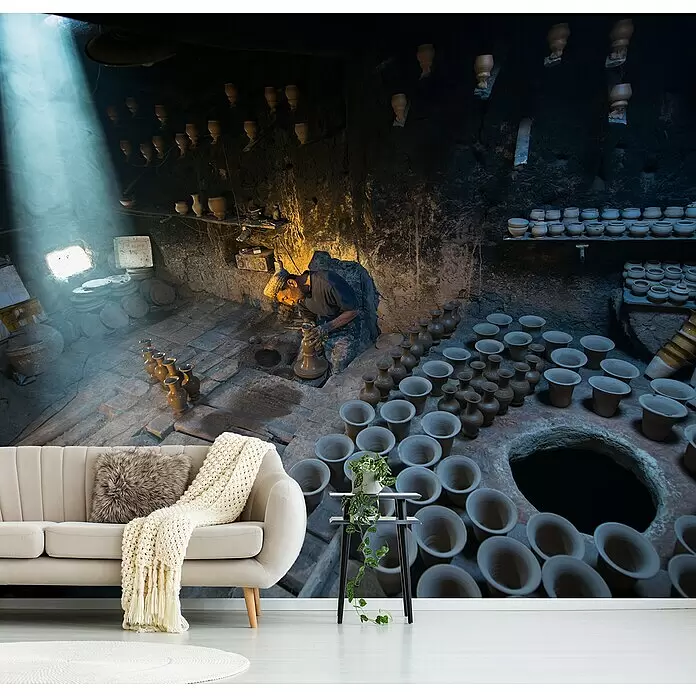 Papermoon Premium collection Fototapete Töpfern im Dachgeschoss - B x H: 250 x 186 cm, Vlies - Helles beiges Sofa mit Decke und Kissen, schwarzer Beistelltisch mit Topfpflanze vor einer Töpferwerkstatt-Wandmalerei.