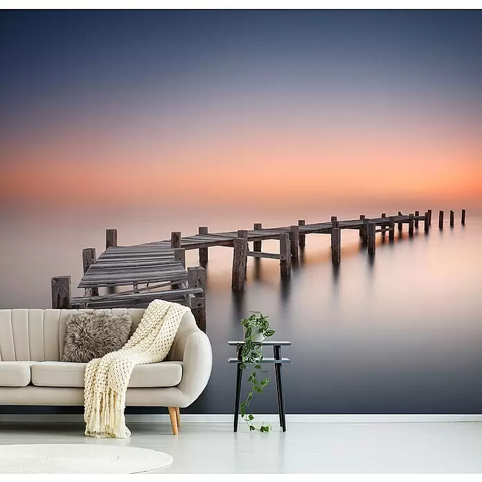 Papermoon Premium collection Fototapete Alter Pier II - B x H: 250 x 186 cm, Vlies - Wandtapete mit ruhigem Sonnenuntergang über dem Wasser und altem Holzsteg, hinter einem modernen Wohnzimmersofa.