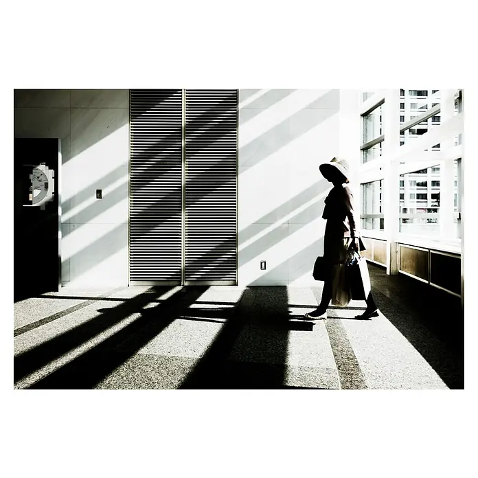 Papermoon Premium collection Fototapete Der Tagtraum - B x H: 300 x 223 cm, Vlies - Silhouette einer Frau mit Hut und Einkaufstüten in einem hellen Gebäude mit starken Licht- und Schattenkontrasten.