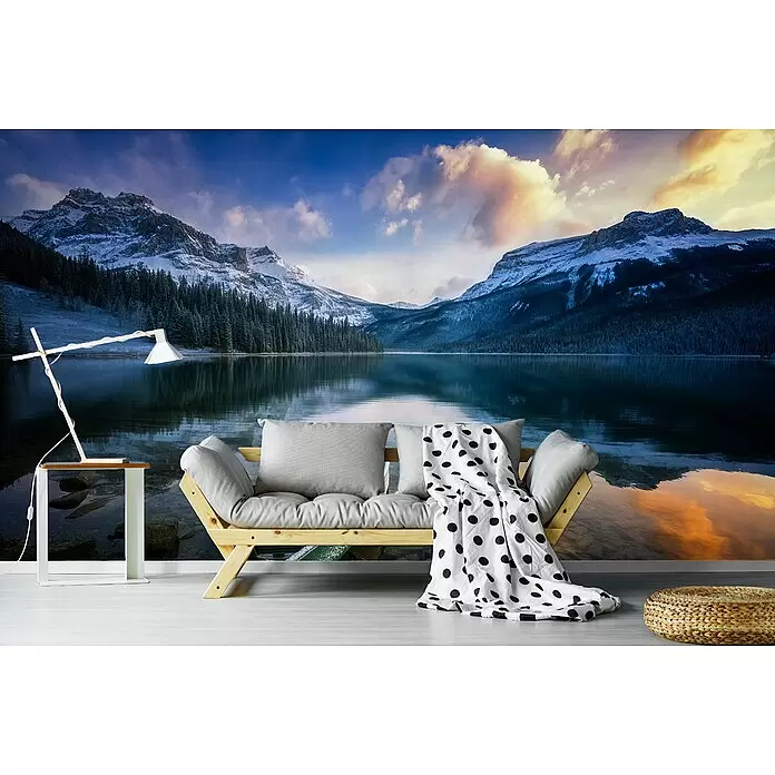 Papermoon Premium collection Fototapete Erster Frost am See - B x H: 250 x 186 cm, Vlies - Helles Holzsofa mit grauen Kissen und gepunkteter Decke in einem Raum mit Bergseewandbild, neben weißer Lampe und geflochtenem Pouf.