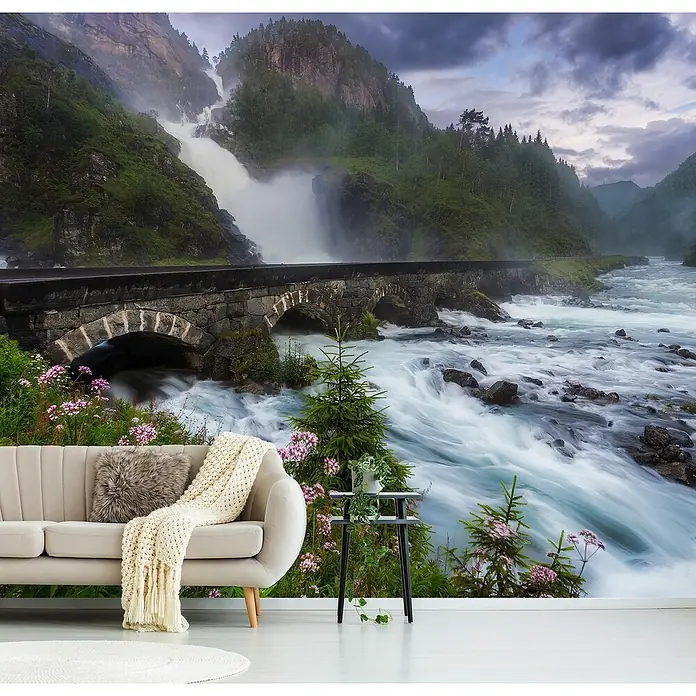 Papermoon Premium collection Fototapete Laytefosse - B x H: 250 x 186 cm, Vlies - Ein gemütliches Wohnzimmer mit einem Wandbild von einem rauschenden Wasserfall unter einer Steinbrücke, das eine ruhige Atmosphäre schafft.