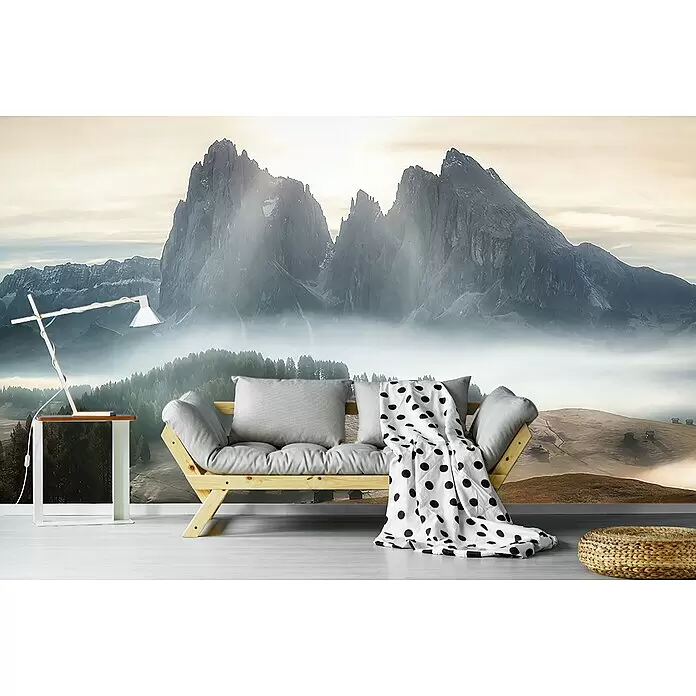 Papermoon Premium collection Fototapete Neblige Berge - B x H: 200 x 149 cm, Vlies - Ein helles Holzsofa mit grauen Kissen und einer weiß-gepunkteten Decke vor einer Berg-Wandtapete.