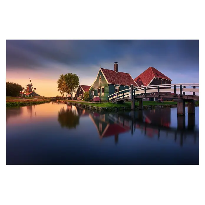 Papermoon Premium collection Fototapete Haus an der Zaan - B x H: 300 x 223 cm, Vlies - Windmühle & grüne Häuser mit roten Dächern, verbunden durch eine Brücke, spiegeln sich im ruhigen Wasser unter einem bunten Himmel.