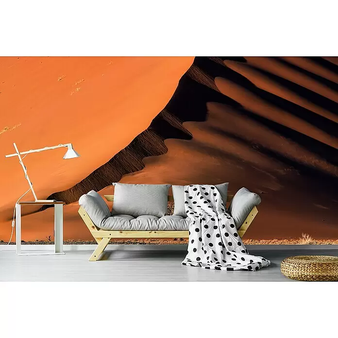 Papermoon Premium collection Fototapete Düne und Baum - B x H: 500 x 280 cm, Vlies - Ein Holzsofa mit hellgrauen Kissen und einer schwarz-weiß gepunkteten Decke, in einem Raum mit Wüstendünen-Wandbild.
