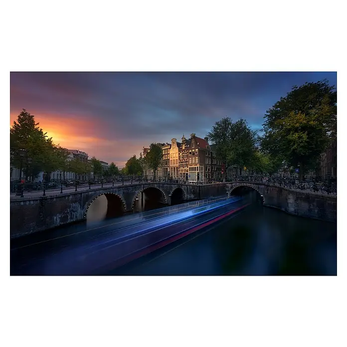 Papermoon Premium collection Fototapete Amsterdam Sunset - B x H: 500 x 280 cm, Vlies - Abenddämmerung in Amsterdam: Kanal mit Brücke und verschwommenen Lichtern eines vorbeifahrenden Bootes unter einem bunten Himmel.