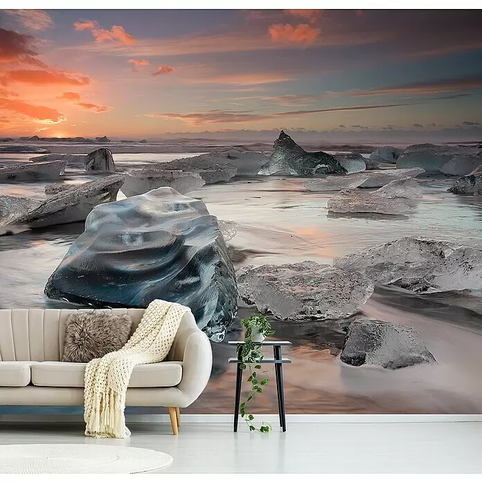 Papermoon Premium collection Fototapete Glacial Lagoon Beach - B x H: 450 x 280 cm, Vlies - Große Wandtapete mit lebhaftem Sonnenuntergang über einem eisigen Strand mit Eisbergen, installiert in einem gemütlichen Wohnzimmer hinter einem hellen Sofa.