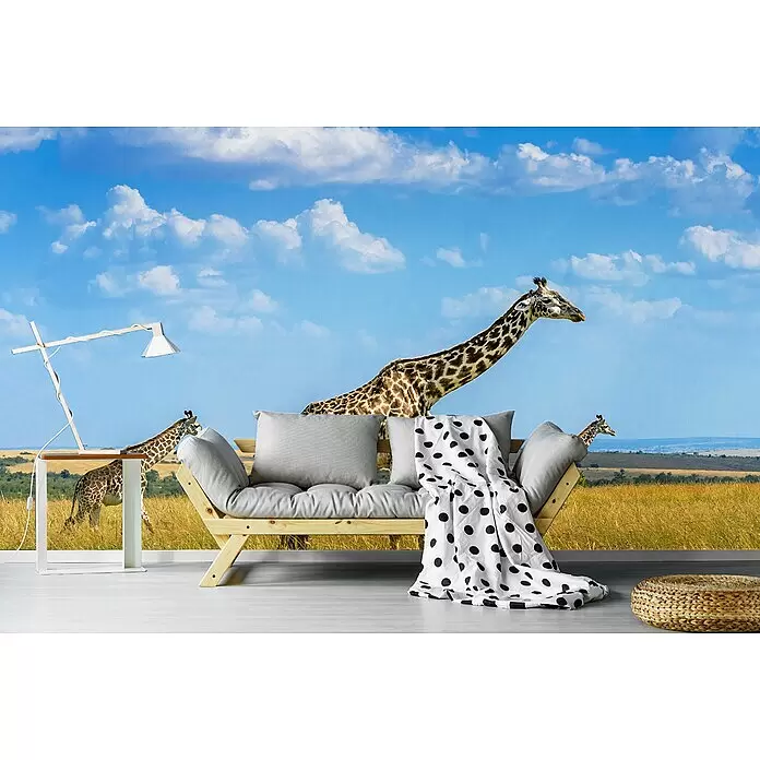 Papermoon Premium collection Fototapete Trio-Giraffen - B x H: 250 x 186 cm, Vlies - Ein helles Holzsofa mit grauen Kissen und einer weiß-gepunkteten Decke in einem Raum mit Giraffen-Wandbild.