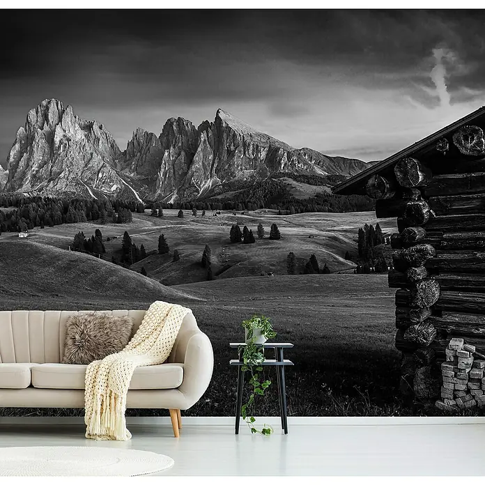 Papermoon Premium collection Fototapete Berghütte - B x H: 350 x 260 cm, Vlies - Ein elegantes Sofa mit Kissen und Decke vor einer Berglandschaft-Fototapete, die das Wohnzimmer aufwertet und eine gemütliche Atmosphäre schafft.