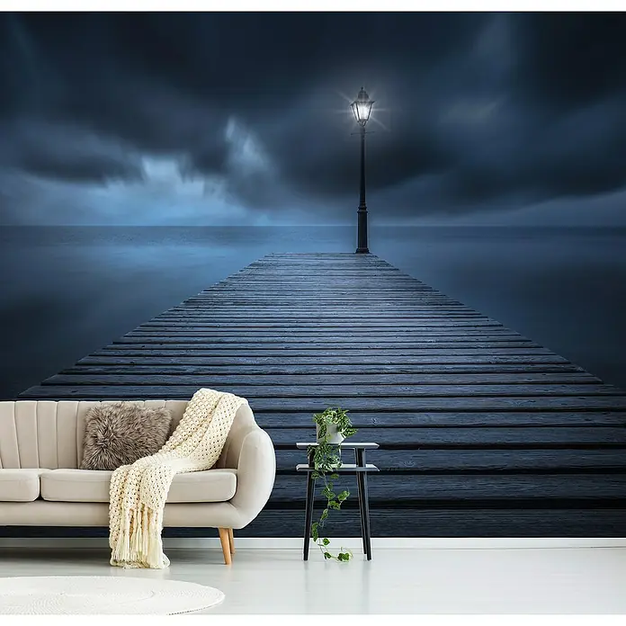 Papermoon Premium collection Fototapete Erste Lichter - B x H: 500 x 280 cm, Vlies - Wohnzimmer mit einem Sofa, einem Beistelltisch und einer Fototapete mit einem Pier und einem Leuchtturm, die eine gemütliche und ruhige Atmosphäre schaffen.