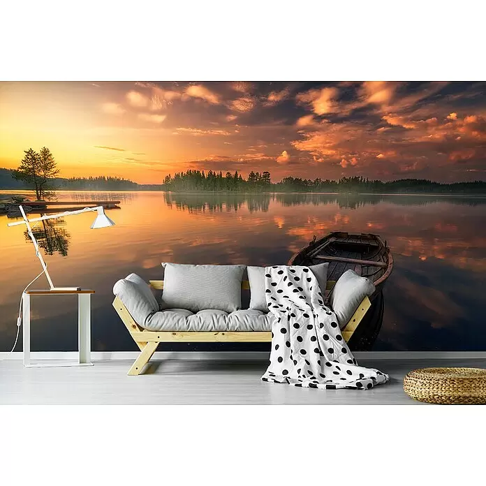 Papermoon Premium collection Fototapete Ziele - B x H: 350 x 260 cm, Vlies - Ein hölzernes Futonsofa mit hellgrauen Kissen, gepunkteter Decke, weißem Beistelltisch mit Lampe und geflochtenem Pouf in einem Raum mit Seewandbild.